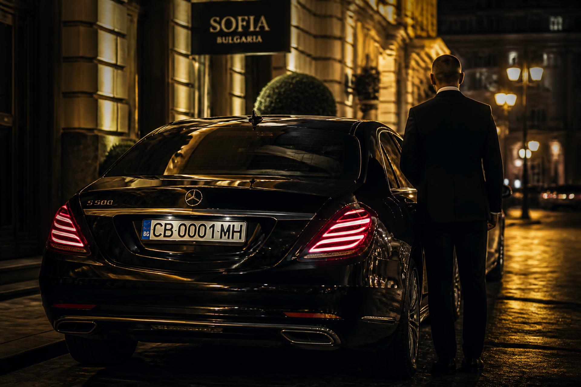 Chauffeur opening the rear door of a black Mercedes S-Class in Sofia at night
